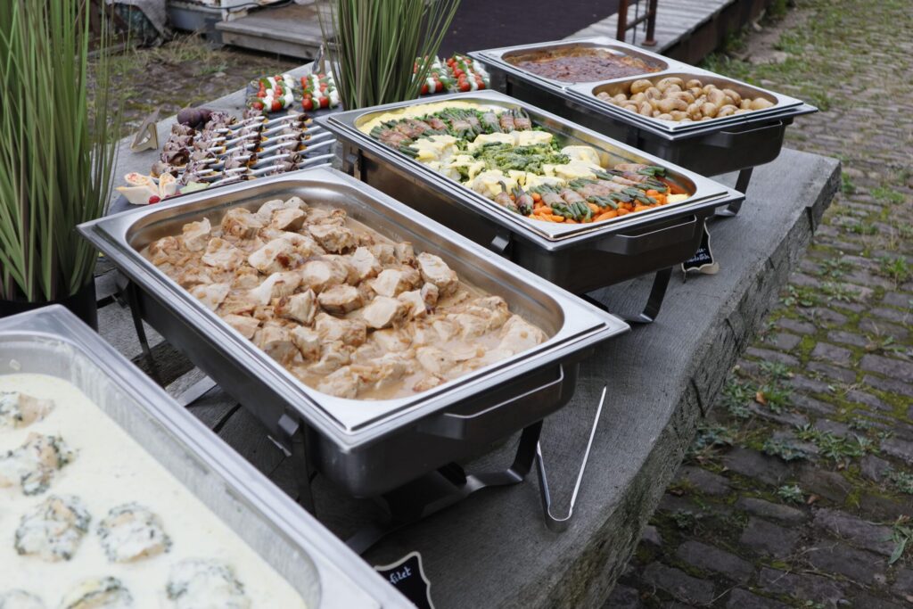 Buffet von Klein Catering mit verschiedenen Hauptgerichten in Warmhaltebehältern, darunter Fleischgerichte, Gemüsebeilagen und Kartoffeln, perfekt angerichtet für Events